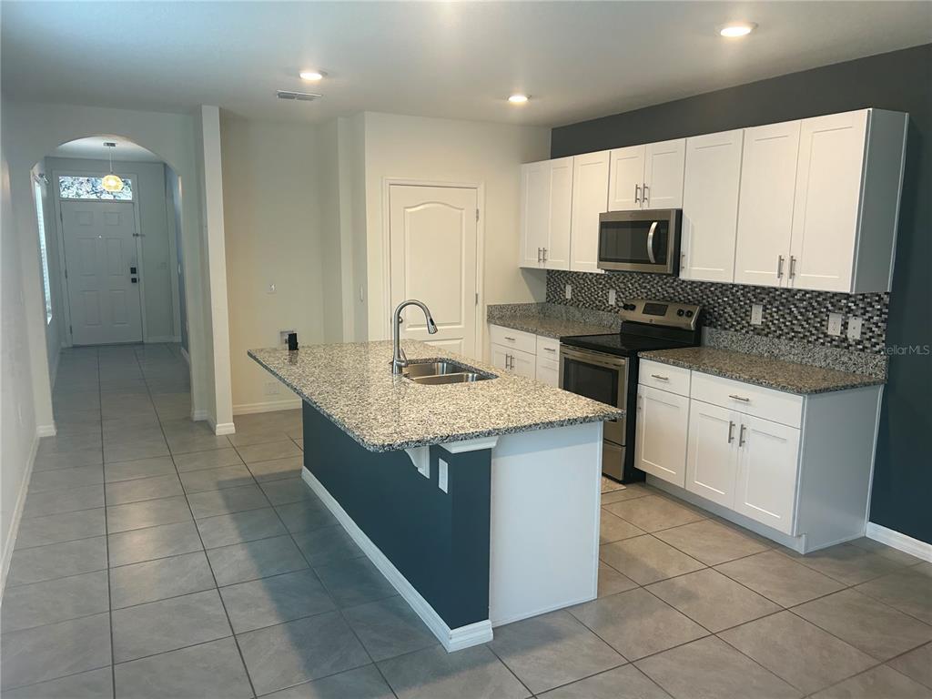 A kitchen features white cabinets, granite countertops, a center island, and gray tile flooring — 462 LIU LANE, DELAND, FL