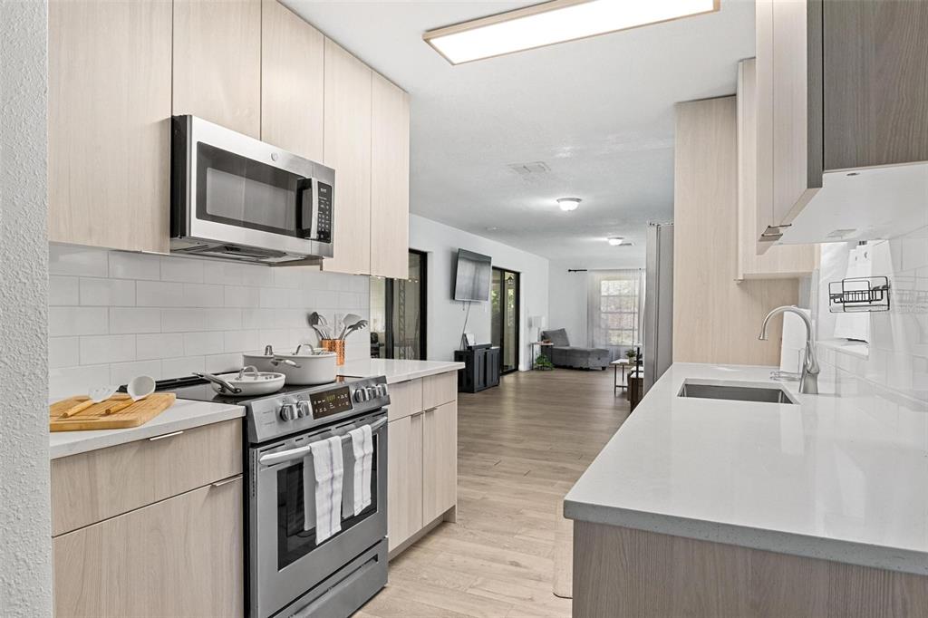 A modern kitchen with light wood cabinets, stainless steel appliances, and white quartz countertops — 919 AVENUE S SE, WINTER HAVEN, FL