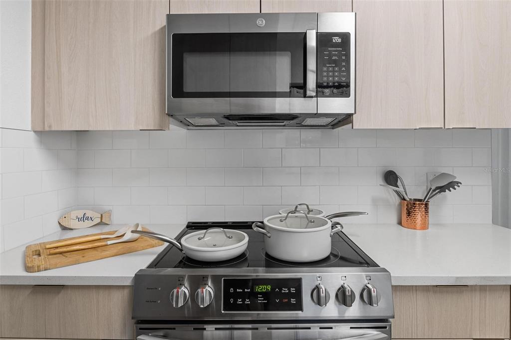A modern kitchen features light wood cabinets, a stainless steel microwave, and a glass-top stove — 919 AVENUE S SE, WINTER HAVEN, FL