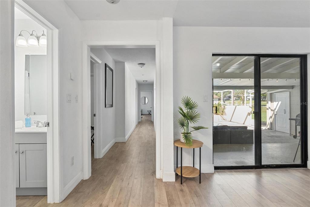 A hallway with light wood flooring leads to a bathroom and a sliding glass door — 919 AVENUE S SE, WINTER HAVEN, FL