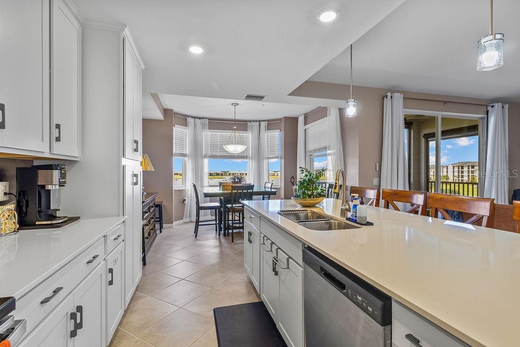A kitchen with white cabinets and a large island overlooks a dining area and balcony — 5651 DOUBLE EAGLE CIRCLE UNIT 4336, AVE MARIA, FL