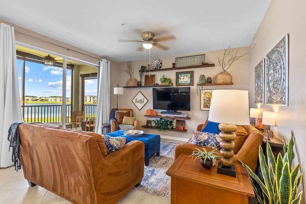 A living room features brown sofas, a blue ottoman, wall shelving, and a balcony view — 5651 DOUBLE EAGLE CIRCLE UNIT 4336, AVE MARIA, FL