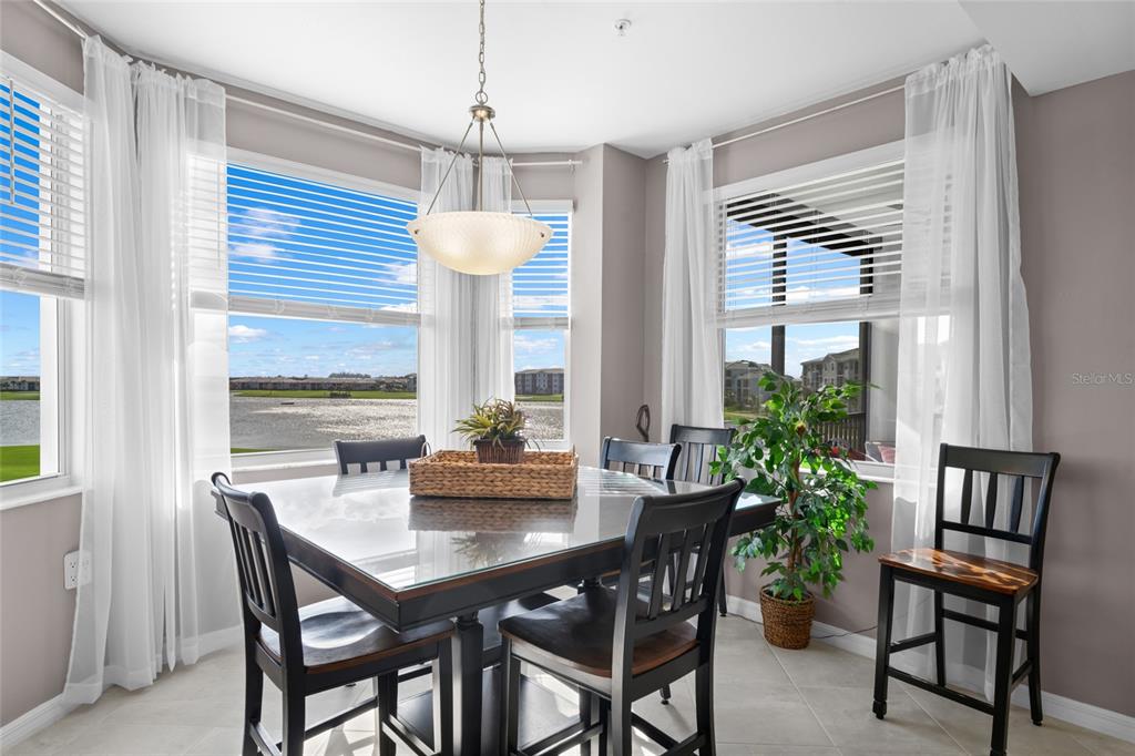 A dining area features a glass-topped table, black chairs, and large windows overlooking a lake — 5651 DOUBLE EAGLE CIRCLE UNIT 4336, AVE MARIA, FL