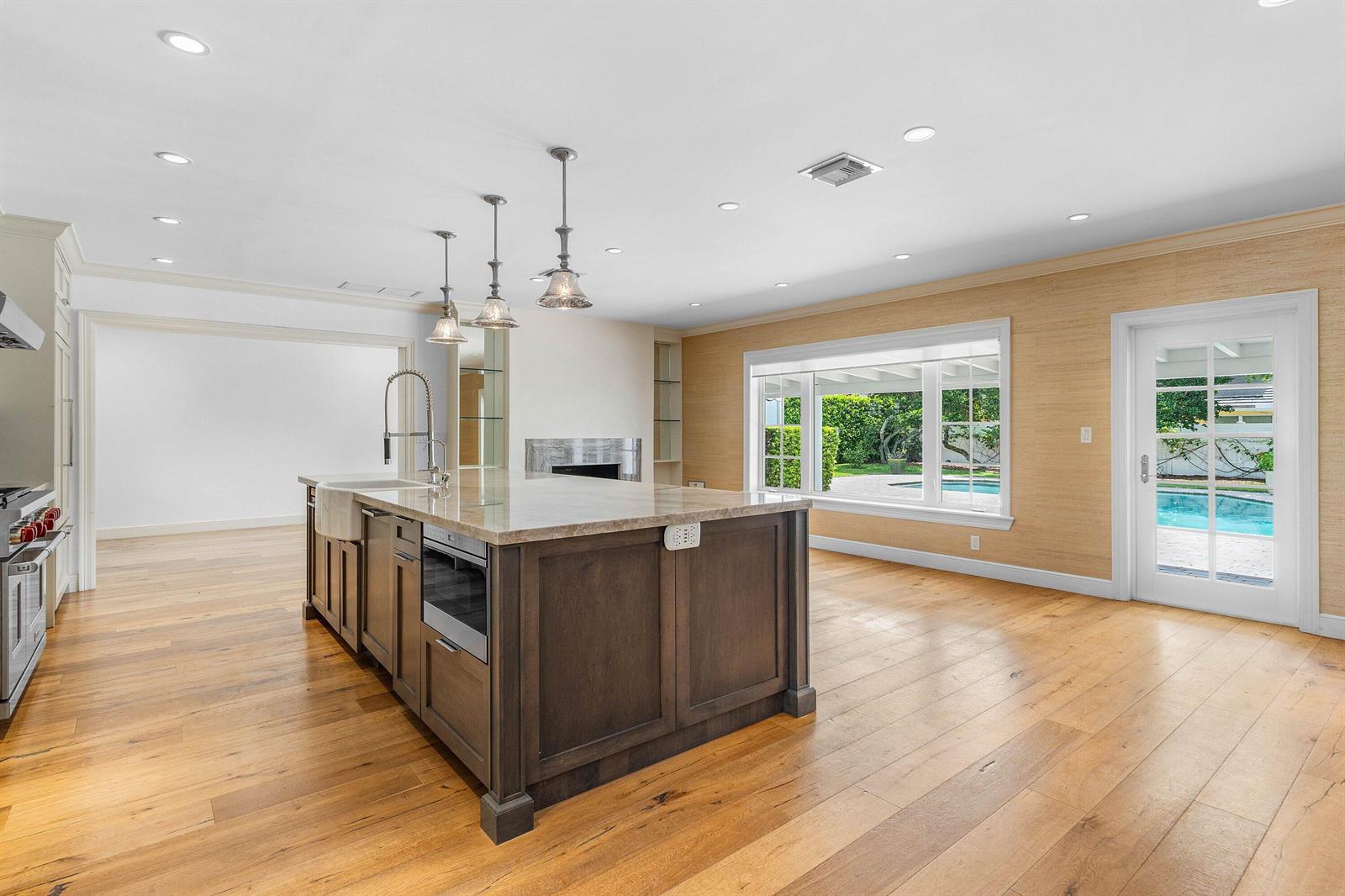 A kitchen with a dark wood island, stone countertops, and hardwood floors overlooks a pool — 1103 NW 6th Avenue, Delray Beach FL 33444, DELRAY BEACH, FL