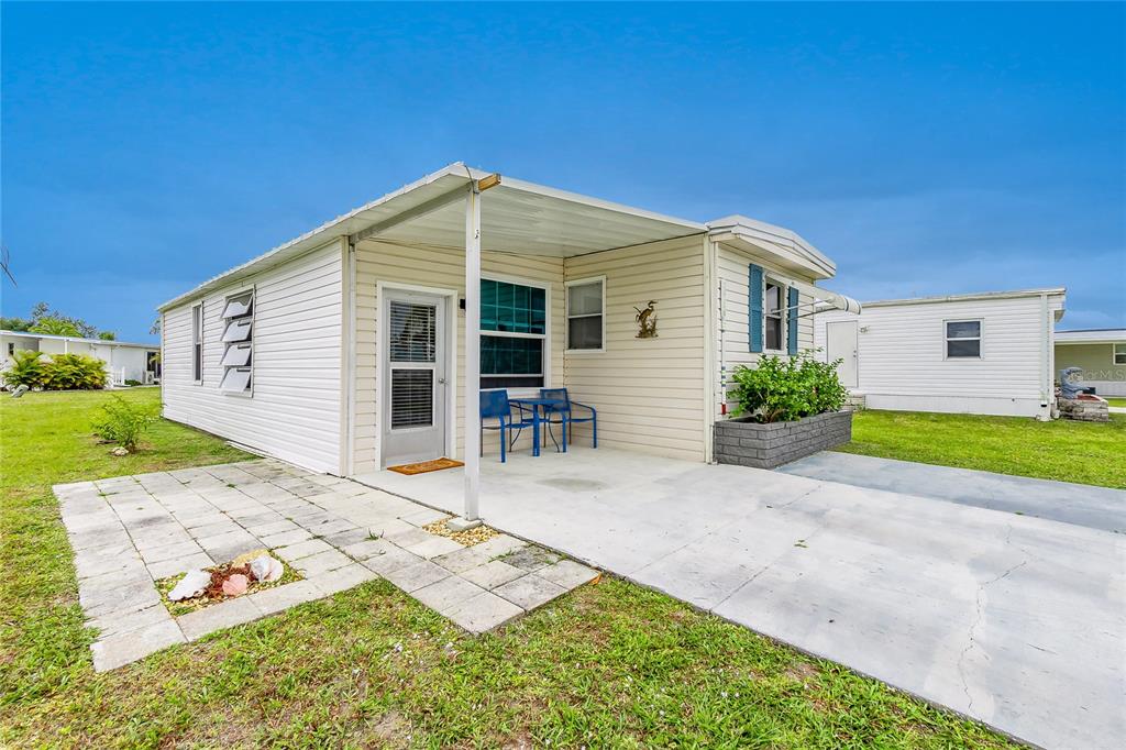 A single-story mobile home with a covered concrete patio and a small stone walkway — 7436 ARBELA STREET, PORT CHARLOTTE, FL