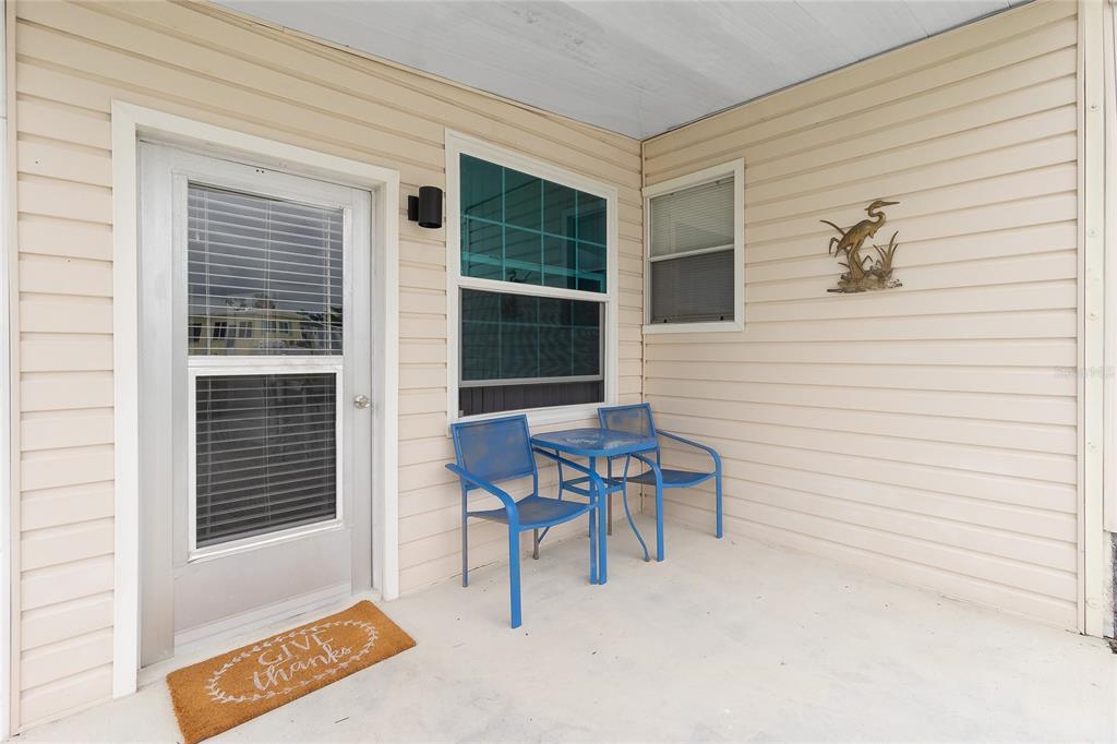 A covered porch features beige vinyl siding, a glass-paneled door, two blue chairs, and a table — 7436 ARBELA STREET, PORT CHARLOTTE, FL