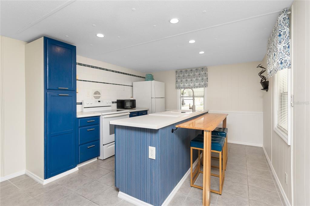 A kitchen with blue cabinets, a white island, a wooden breakfast bar, and tile flooring — 7436 ARBELA STREET, PORT CHARLOTTE, FL
