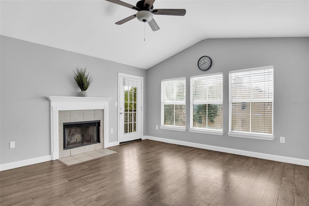 A living room features a fireplace, wood-look flooring, a ceiling fan, and three large windows — 18245 BRIDLE CLUB DRIVE, TAMPA, FL