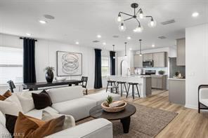 An open-concept living room and kitchen featuring light wood floors and modern light fixtures — 1220 Caloosa Creek Drive, FL 33935, FL