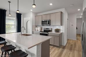 A modern kitchen features light-colored cabinetry, a large quartz island, and stainless steel appliances — 1220 Caloosa Creek Drive, FL 33935, FL