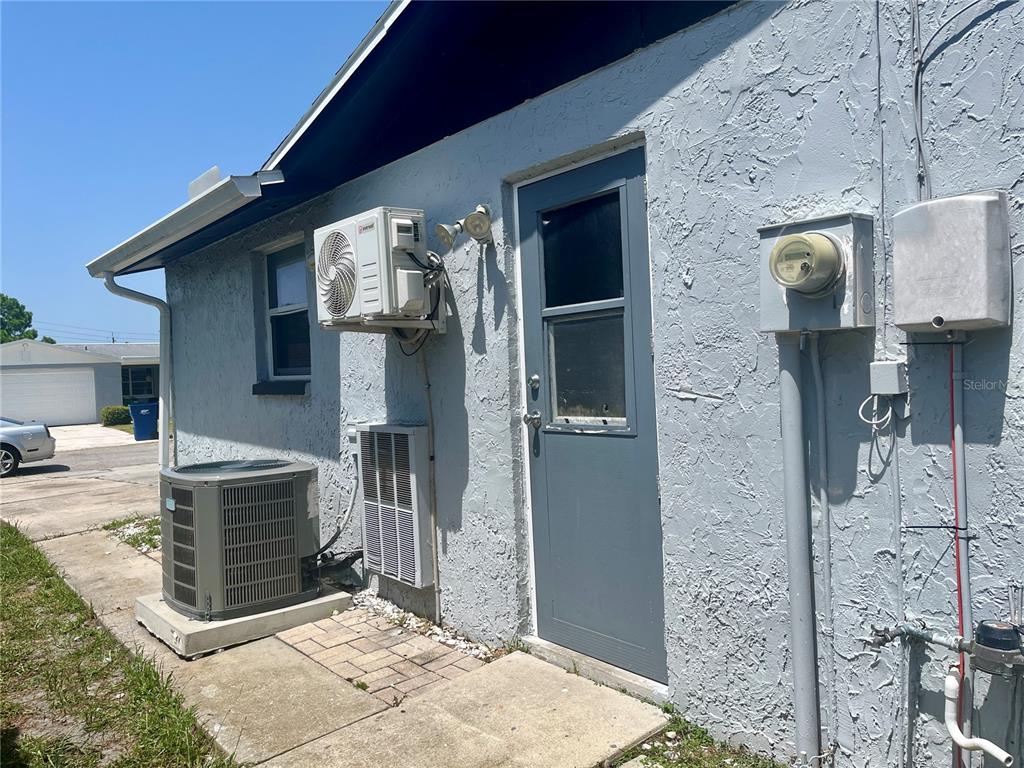 The exterior of a house features a gray door, an air conditioning unit, and a meter — 3716 CEDARWOOD DRIVE, HOLIDAY, FL