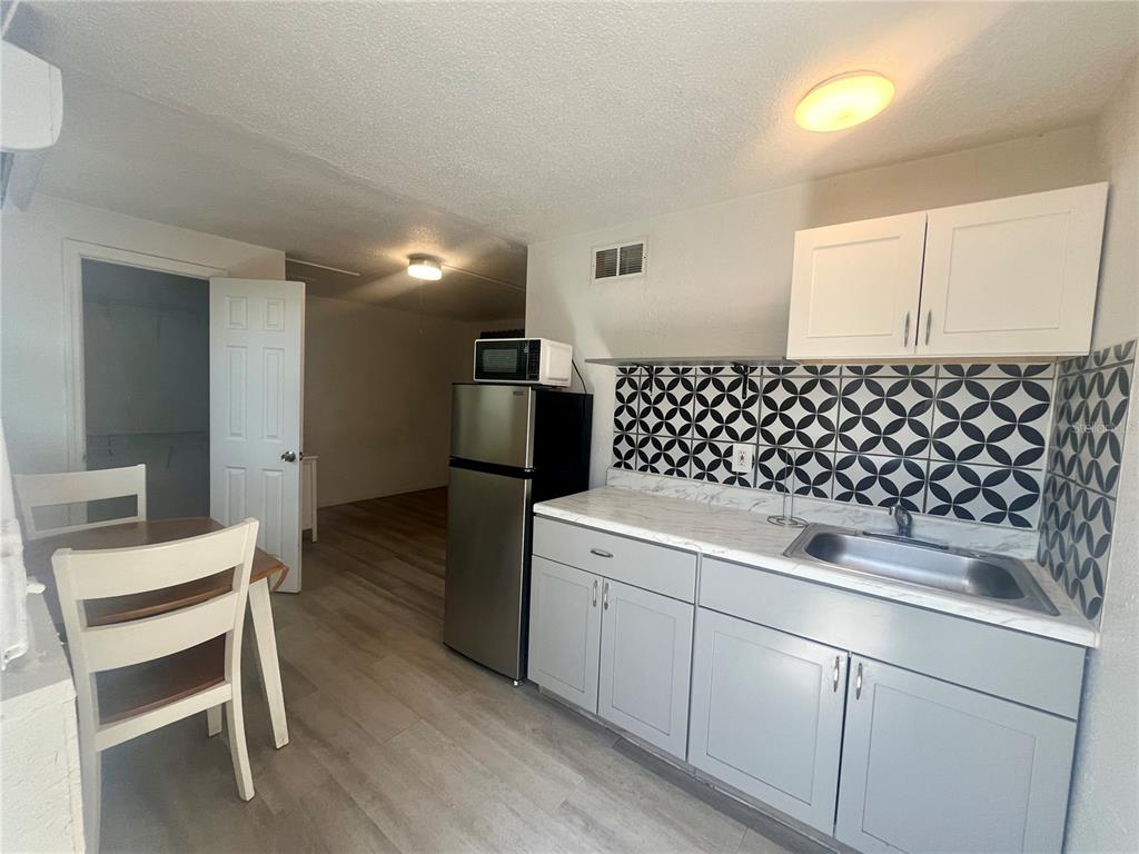 A kitchen features gray cabinets, a stainless steel refrigerator, and a black-and-white patterned backsplash — 3716 CEDARWOOD DRIVE, HOLIDAY, FL