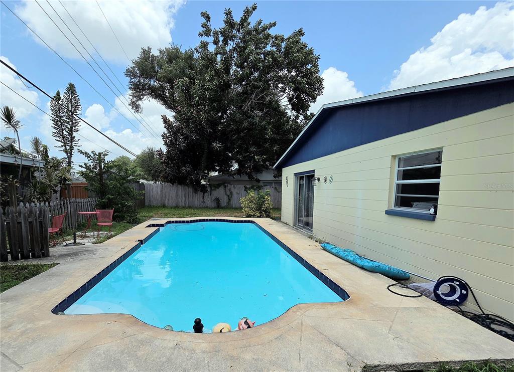 A backyard swimming pool sits next to a light yellow house with a blue roof — 9272 51ST STREET N, PINELLAS PARK, FL