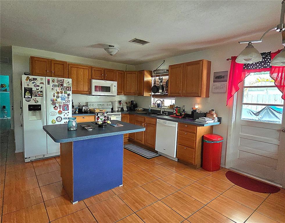 A kitchen features wood cabinets, a blue island, tile flooring, and white appliances — 9272 51ST STREET N, PINELLAS PARK, FL