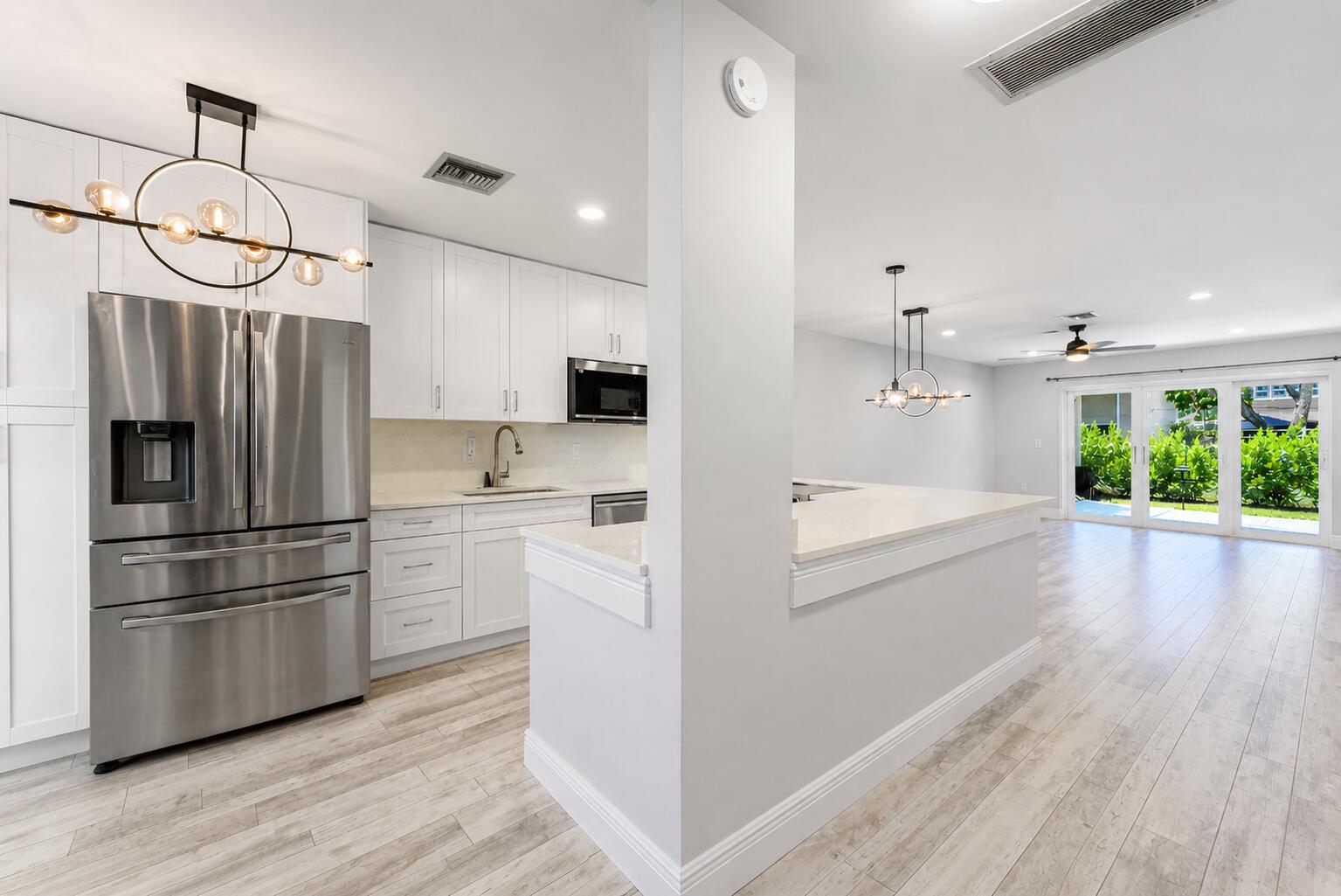 A modern kitchen with white cabinets, stainless steel appliances, and a peninsula overlooks a living area — 13788 Via Flora # B, Delray Beach FL 33484, DELRAY BEACH, FL