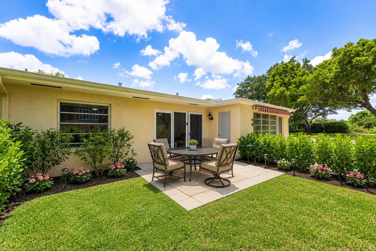 A patio with a dining set sits on a lawn behind a yellow house — 13788 Via Flora # B, Delray Beach FL 33484, DELRAY BEACH, FL