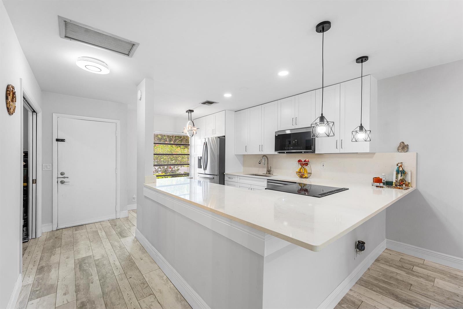 A modern kitchen features white cabinets, quartz countertops, stainless steel appliances, and wood-look tile flooring — 13788 Via Flora # B, Delray Beach FL 33484, DELRAY BEACH, FL
