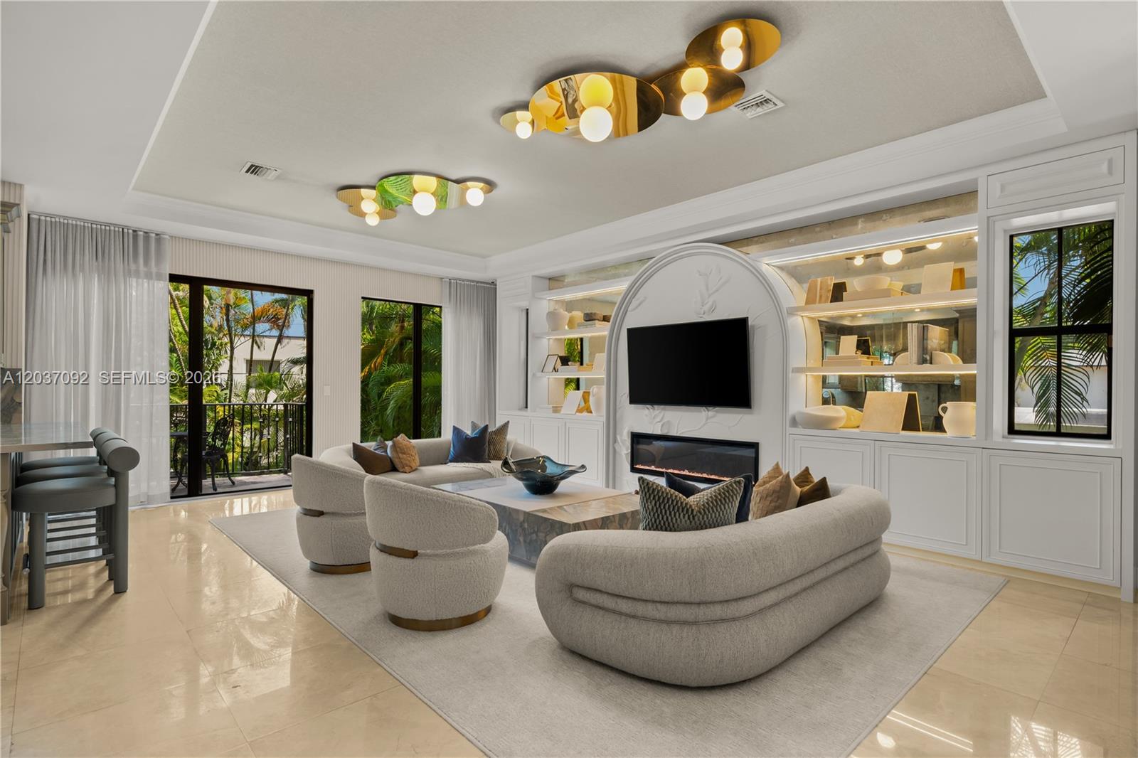 A modern living room features a fireplace, built-in shelving, curved furniture, and gold ceiling fixtures — 1803 S Bayshore Ln, Miami FL 33133, MIAMI, FL