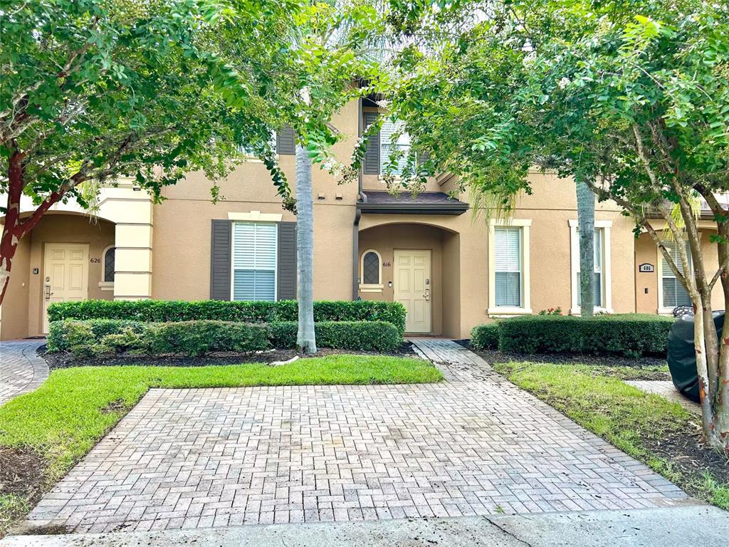 A tan two-story townhouse exterior features a brick paver driveway and manicured hedges — 616 VERONA AVE, DAVENPORT, FL