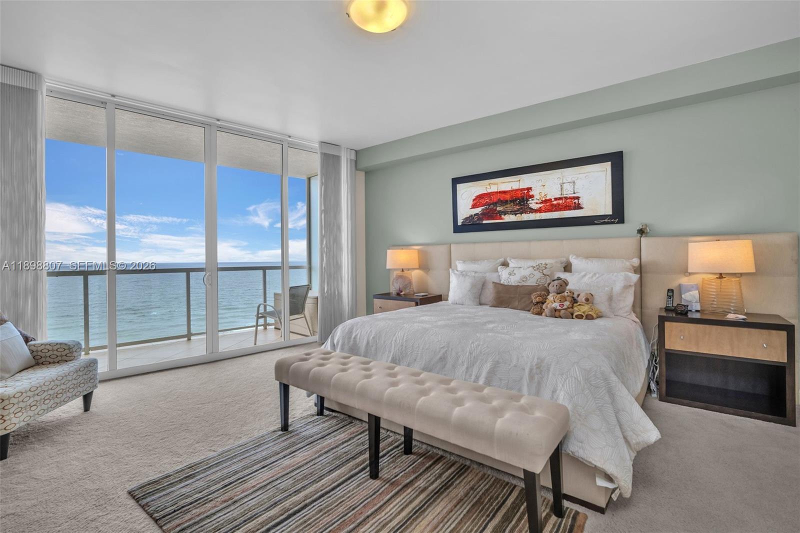 A bedroom features a king bed, a tufted bench, and a balcony overlooking the ocean — 704 N Ocean Blvd # 804, Pompano Beach FL 33062, POMPANO BEACH, FL