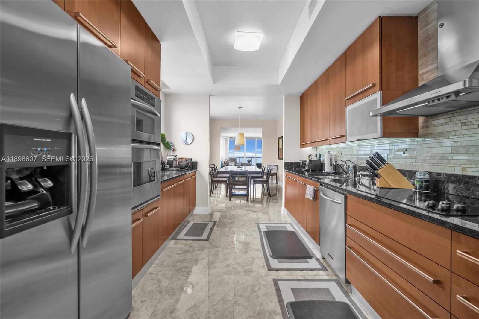 A galley kitchen features wood cabinetry, stainless steel appliances, and dark granite countertops — 704 N Ocean Blvd # 804, Pompano Beach FL 33062, POMPANO BEACH, FL