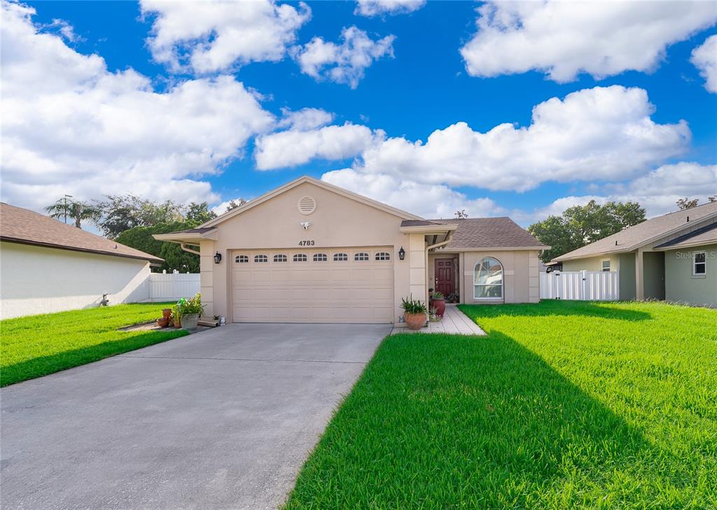 A single-story house with a beige stucco exterior, a two-car garage, and a green lawn — 4783 WARRIOR LANE, KISSIMMEE, FL