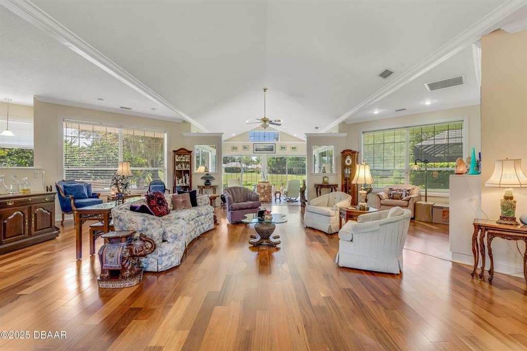 A spacious living room features vaulted ceilings, hardwood floors, and large windows overlooking a backyard — 203 PRESTWICK DRIVE, NEW SMYRNA BEACH, FL