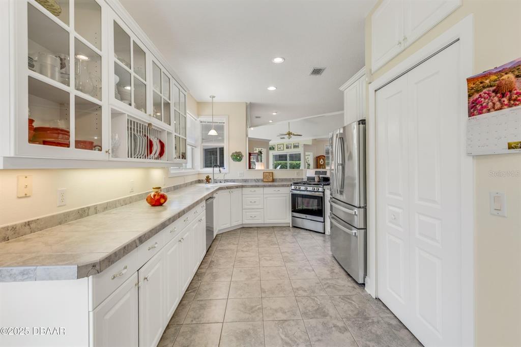 A kitchen features white cabinetry, stainless steel appliances, and light-colored countertops with tile flooring — 203 PRESTWICK DRIVE, NEW SMYRNA BEACH, FL