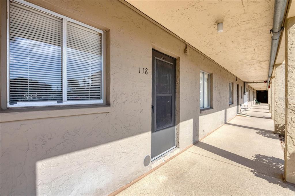 An exterior view of an apartment building walkway with unit 118 and a screened door — 3534 LAKE BAYSHORE DRIVE UNIT K118, BRADENTON, FL