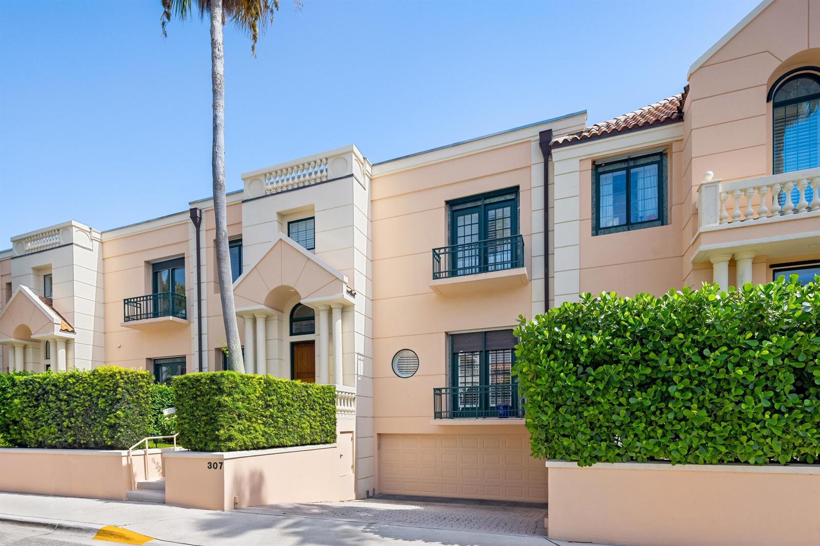 A multi-story peach-colored townhouse features a garage, balconies, and a manicured hedge — 307 Everglade Avenue, Palm Beach FL 33480, PALM BEACH, FL