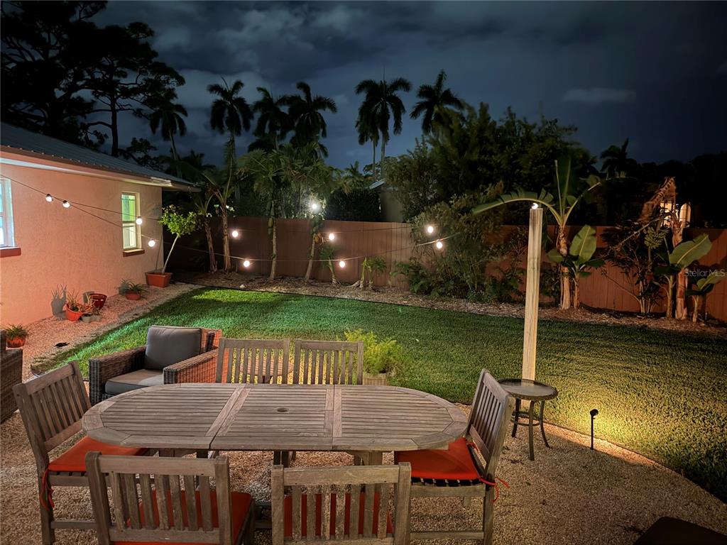A backyard patio features a wooden dining set, string lights, and a grassy lawn at night — 4620 7TH AVENUE W, BRADENTON, FL