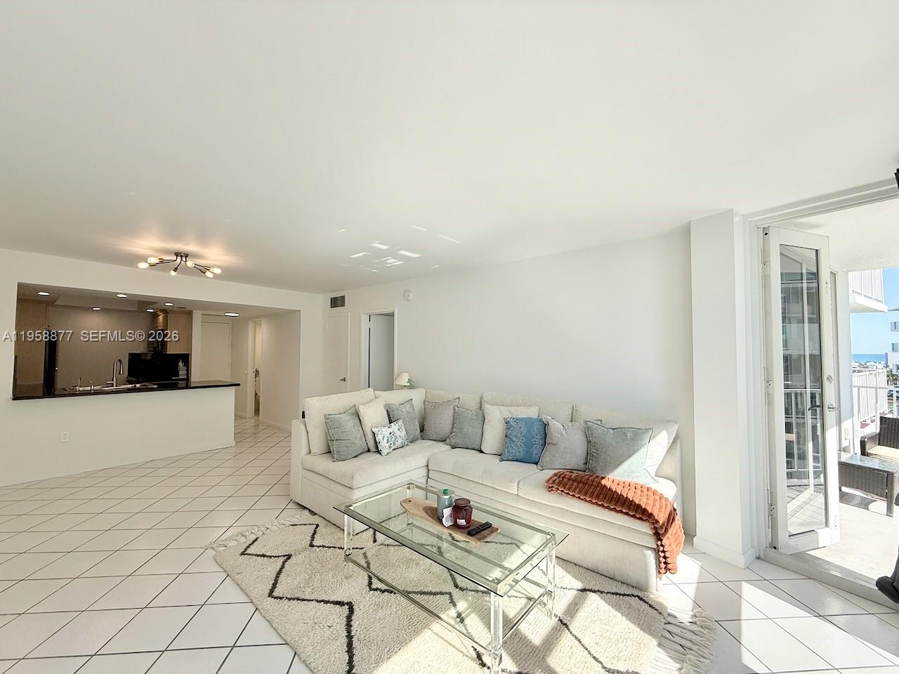 A living room with a white sectional sofa, glass coffee table, and tiled floors — 1228 West Ave # 1415, Miami Beach FL 33139, MIAMI BEACH, FL