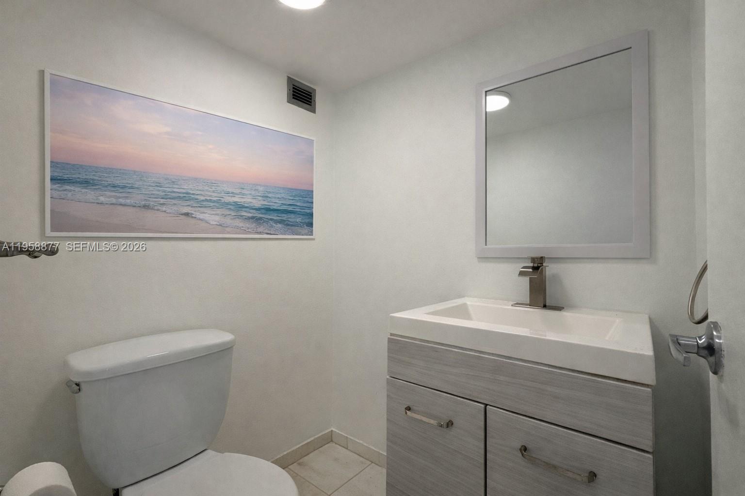 A bathroom features a white toilet, a wood-grain vanity with a sink, and wall art — 1228 West Ave # 1415, Miami Beach FL 33139, MIAMI BEACH, FL
