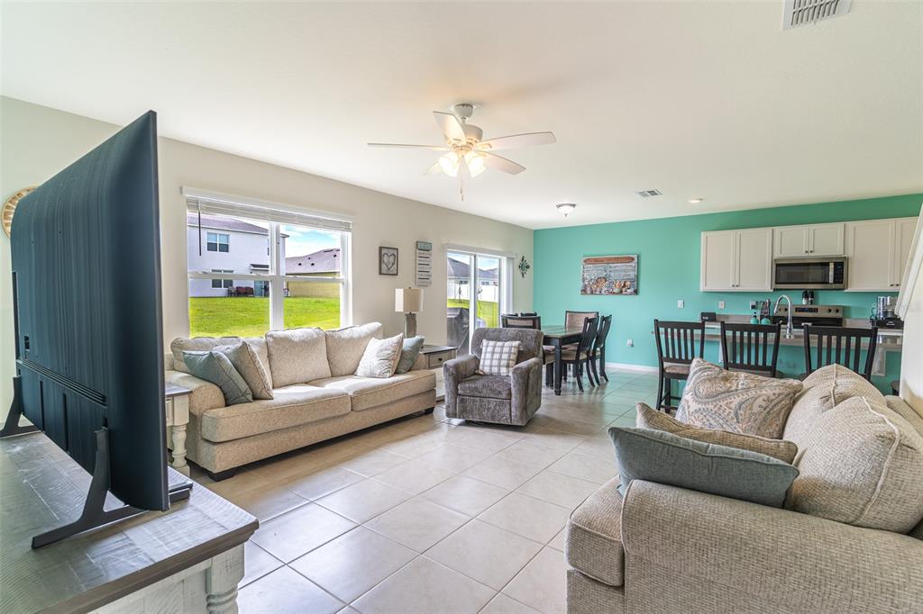 An open-concept living room and kitchen area features tile flooring, a ceiling fan, and furniture — 1328 DAISY FIELD DRIVE, WINTER HAVEN, FL