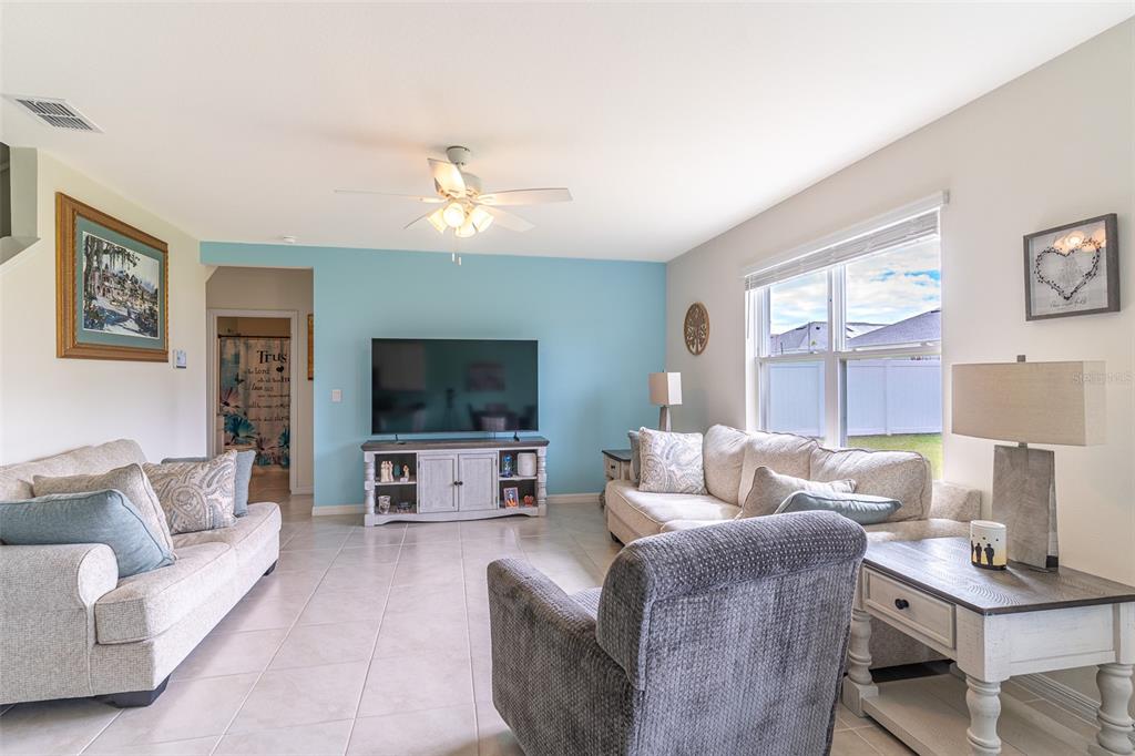 A living room features a light blue accent wall, tile flooring, and neutral-toned furniture — 1328 DAISY FIELD DRIVE, WINTER HAVEN, FL