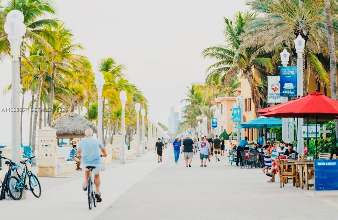 A paved boardwalk lined with palm trees, street lamps, pedestrians, and outdoor restaurant seating — 1425 Arthur # 514B, Hollywood FL 33020, HOLLYWOOD, FL