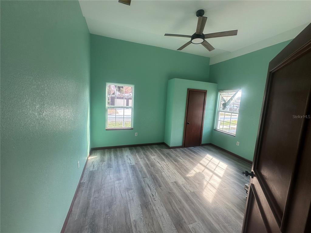 A bedroom with mint green walls, wood-look flooring, a ceiling fan, and two windows — 503 N POLK AVENUE, ARCADIA, FL