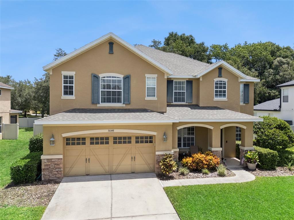 A two-story tan stucco house features a two-car garage, stone accents, and a covered entryway — 30148 JUTLAND COURT, MOUNT DORA, FL
