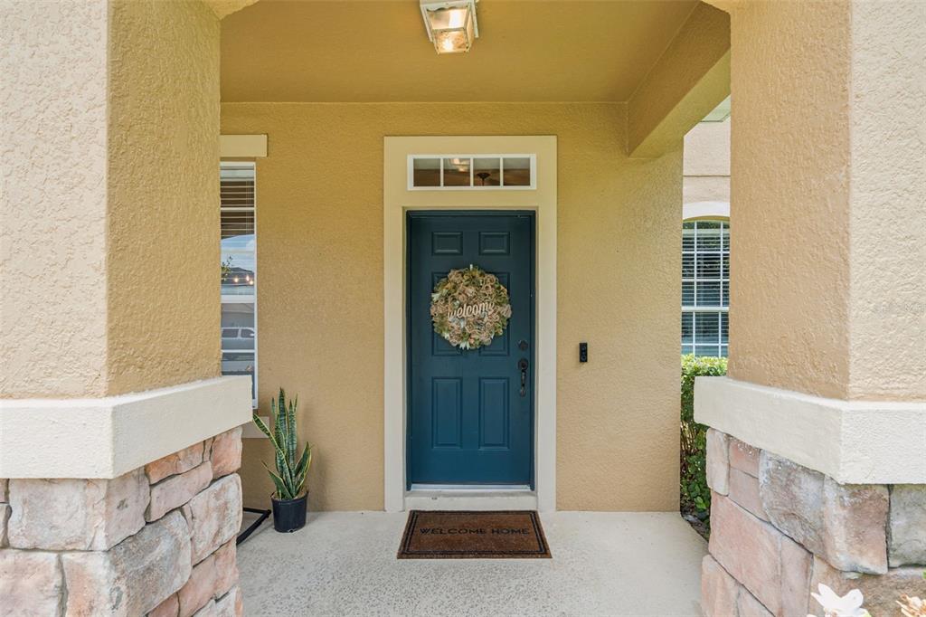 A covered entryway features a blue front door with a wreath and stone-accented columns — 30148 JUTLAND COURT, MOUNT DORA, FL