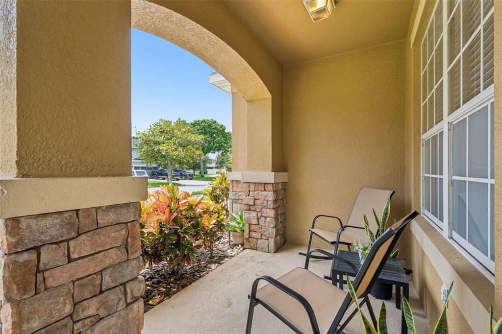 A covered front porch features stone pillars, tan stucco walls, and two chairs — 30148 JUTLAND COURT, MOUNT DORA, FL