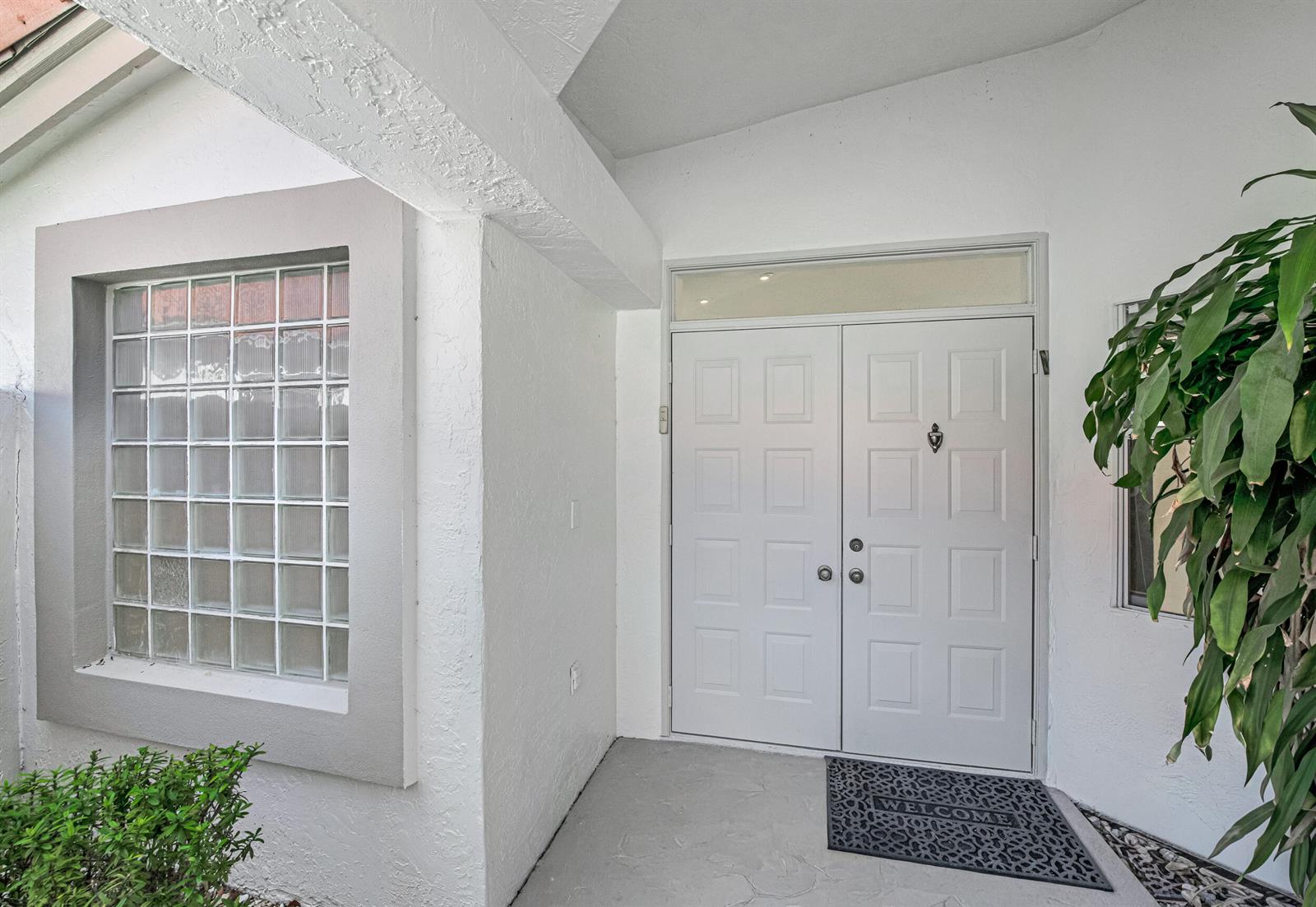 A white double front door with a glass transom sits beside a glass block window — 9758 Harbour Lake Circle, Boynton Beach FL 33437, BOYNTON BEACH, FL