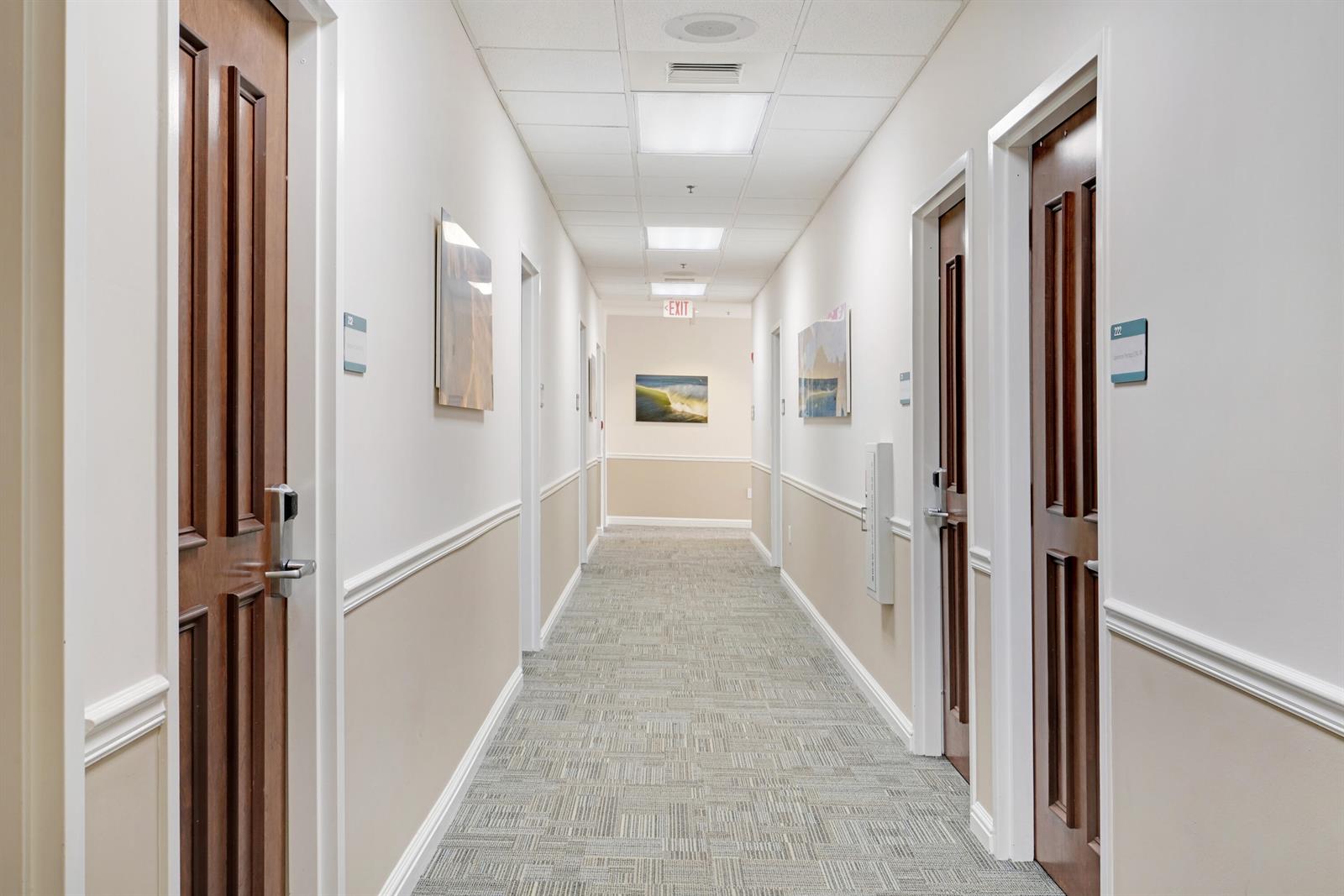 A long office hallway features carpeted flooring, white walls with wainscoting, and several wooden doors — 601 Heritage Drive, Jupiter FL 33458, JUPITER, FL