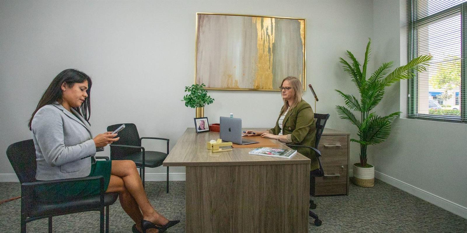 Two women sit in a professional office with a desk, chairs, artwork, and a plant — 601 Heritage Drive, Jupiter FL 33458, JUPITER, FL
