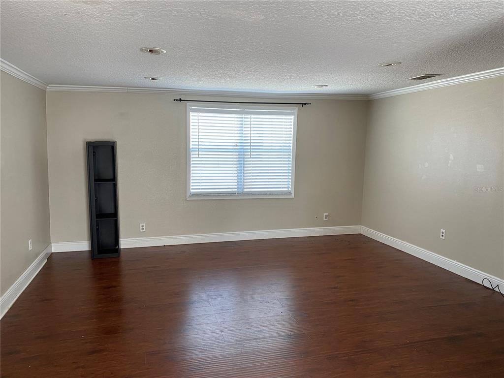 An empty room with dark wood-look flooring, beige walls, and a single window with blinds — 313 S OBSERVATORY DRIVE, ORLANDO, FL