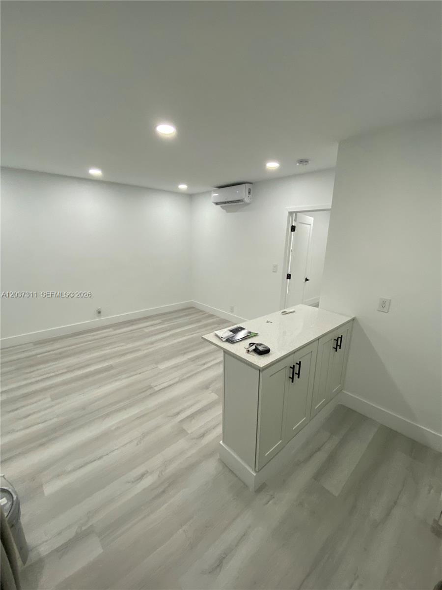 A room with light wood-look flooring features a white kitchen island and a wall-mounted AC — 3071 SW 27th Ave # 4, Miami FL 33133, MIAMI, FL