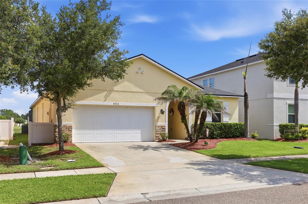 A single-story yellow house with a two-car garage and a palm tree in the yard — 4733 BLUE DIAMOND STREET, KISSIMMEE, FL