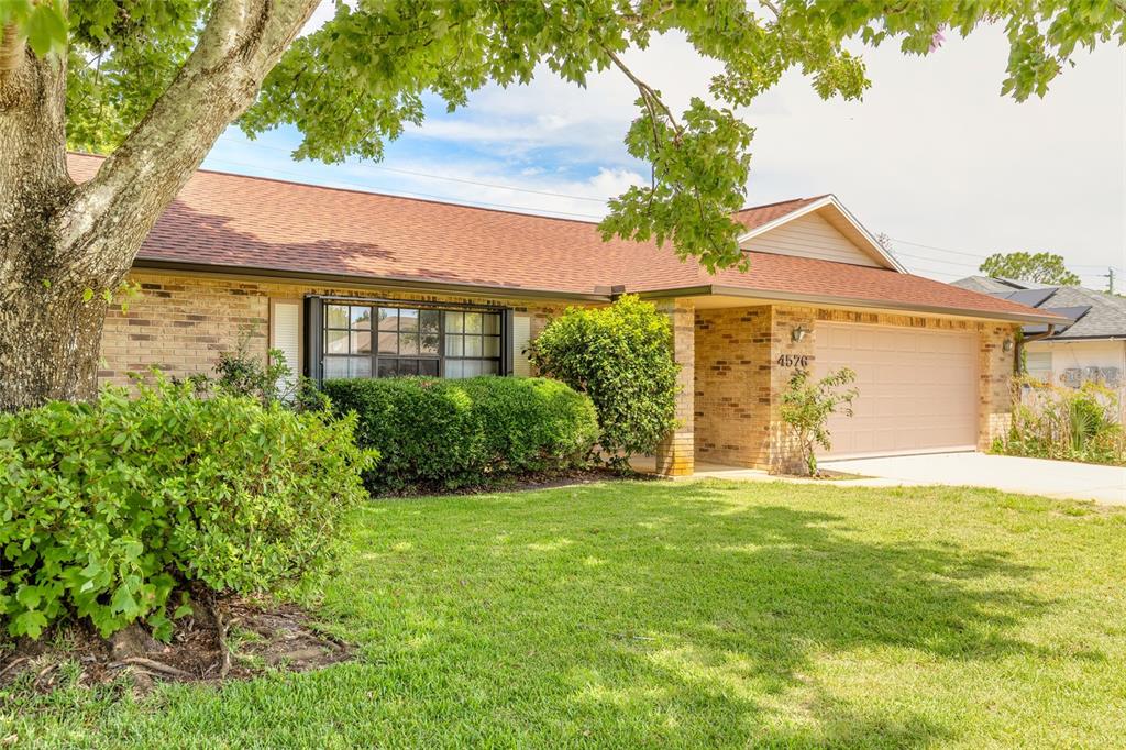 A single-story brick house with a garage and a large tree in the front yard — 4576 PHIPPS DRIVE, PORT ORANGE, FL