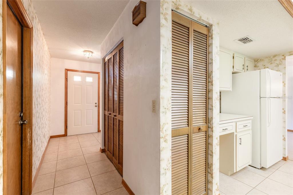 A tiled hallway leads to an entryway door, featuring louvered closet doors and a kitchen area — 4576 PHIPPS DRIVE, PORT ORANGE, FL