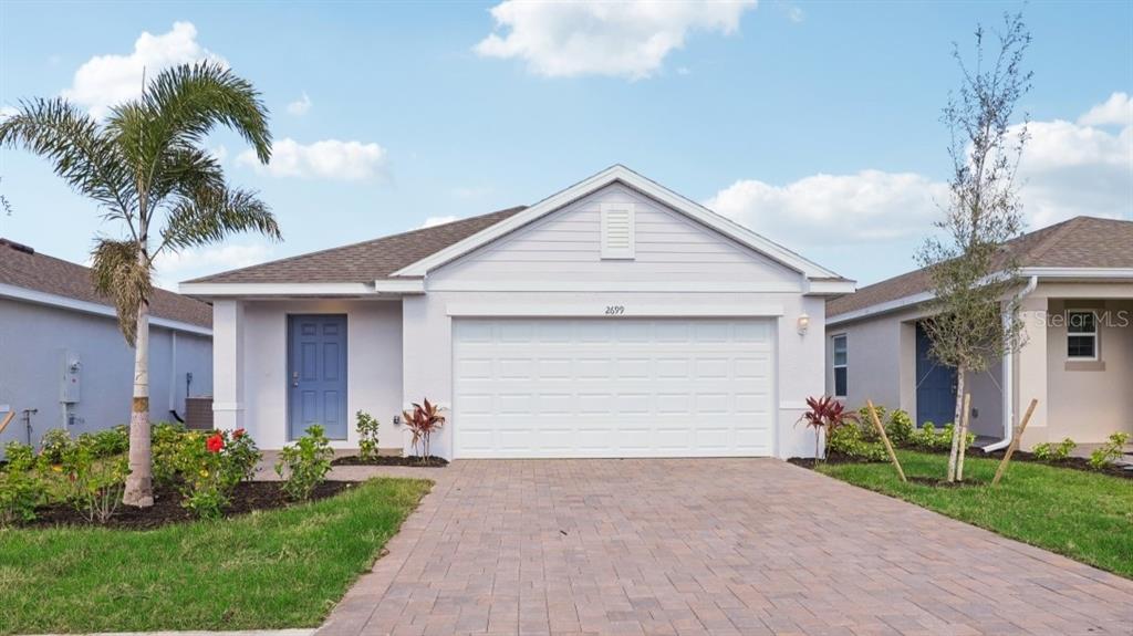 A single-story house with a white garage, blue front door, and a paved driveway — 26199 SACRED LOTUS LANE, PUNTA GORDA, FL