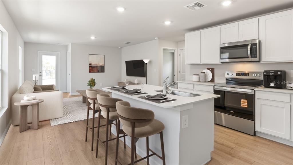 A modern kitchen with white cabinets and an island overlooks a living area with furniture — 26199 SACRED LOTUS LANE, PUNTA GORDA, FL